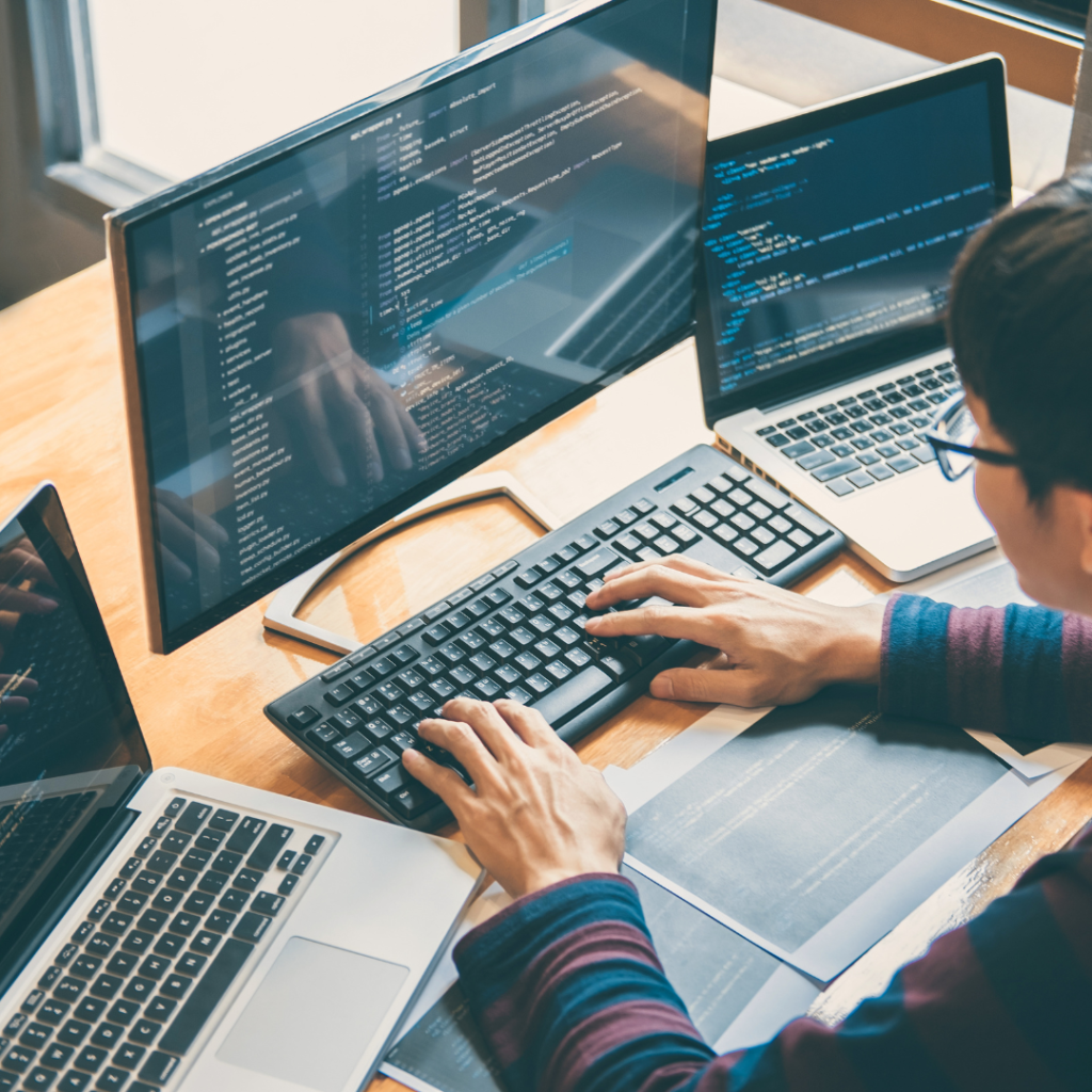 Person typing on a keyboard. There are two open laptops, one on each side of the main PC